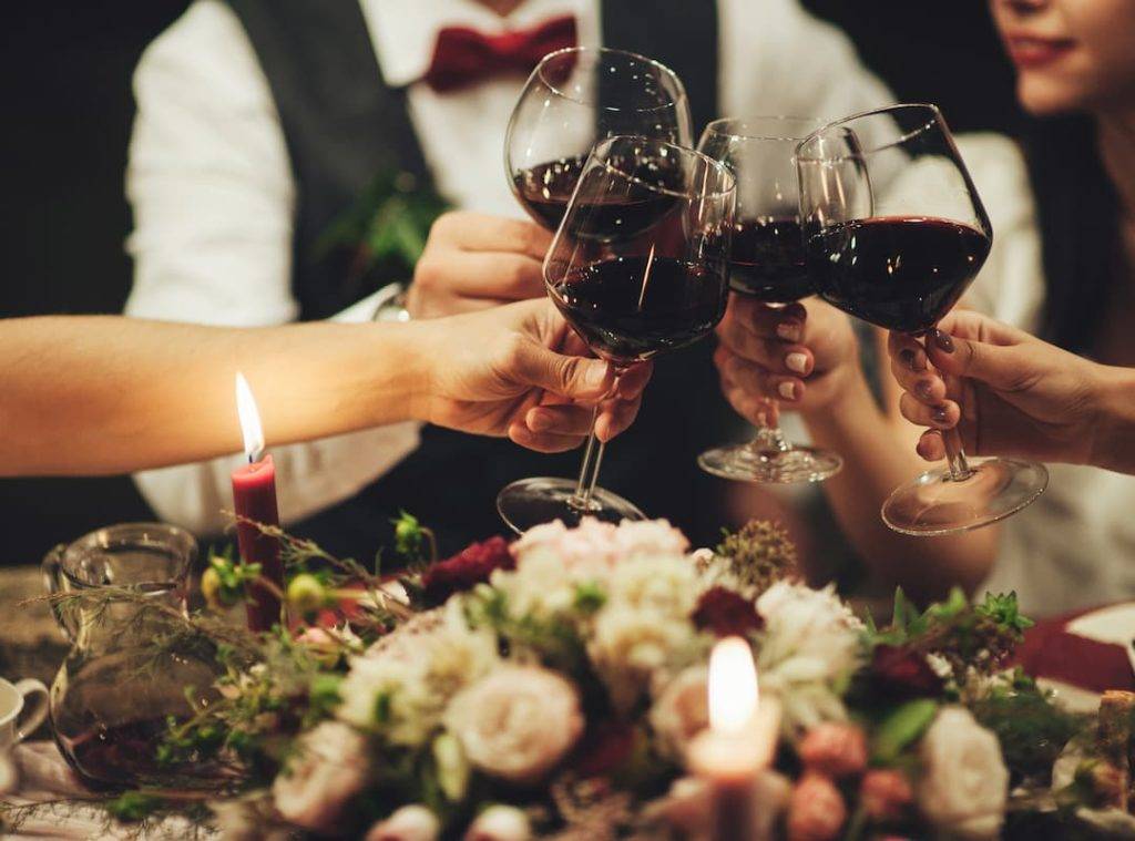 People clang glasses sitting at dinner table in sparkling lights